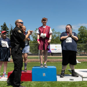 Four athletes on a medal stand with a police officer presenting medals.